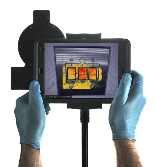 A male wearing blue latex gloves holding a black iPad with the pathfinder attachment showing an image of light switches that have infrared red and yellow colours.