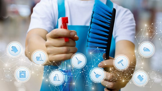 A man in a blue apron and white shirt is holding up a spray bottle with cleaning solution in it, and a clean large bristle brush. Decorative icons litter the front bottom of the page that showcase (left to right) gloves, a dishwasher, mop and bucket, vacuum, broom, traditional broom, large outdoor broom brush, sponge, and an iron.