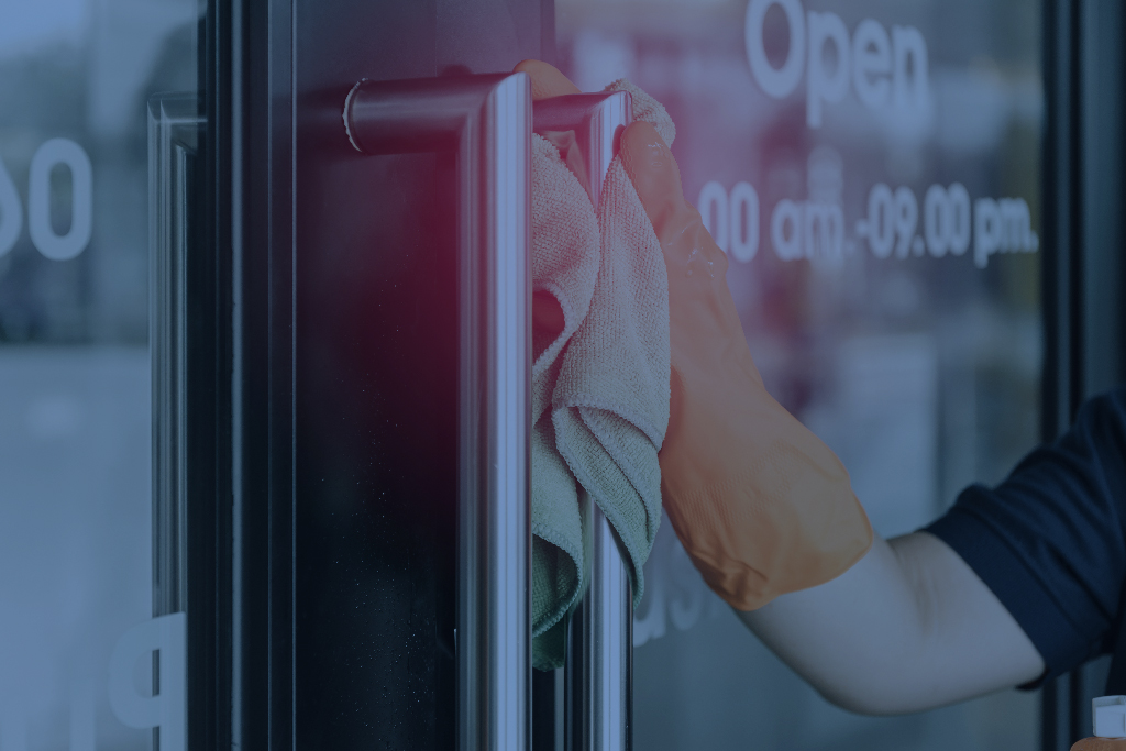 Janitor is using a clean rag to sanitize the door handles of an entry door to an office.