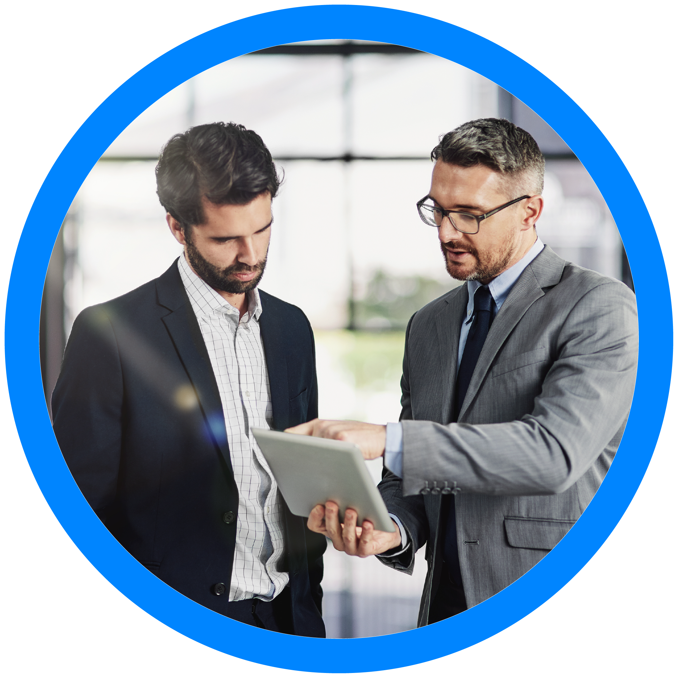 two professional men in a corporate setting, engaged in reviewing data on a tablet. The man on the left, dressed in a dark suit and white shirt, appears to be analyzing the content closely while the other, in a gray suit and glasses, guides or explains the displayed information. The interaction suggests a collaborative effort in business analysis or decision-making, highlighting the use of technology in modern business environments. The circular blue frame around the image emphasizes focus and connectivity, aligning with themes of teamwork and shared objectives.